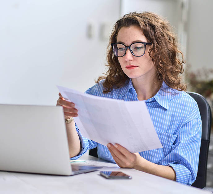 Une femme dans son bureau qui travaille sur un ordinateur et lit des documents